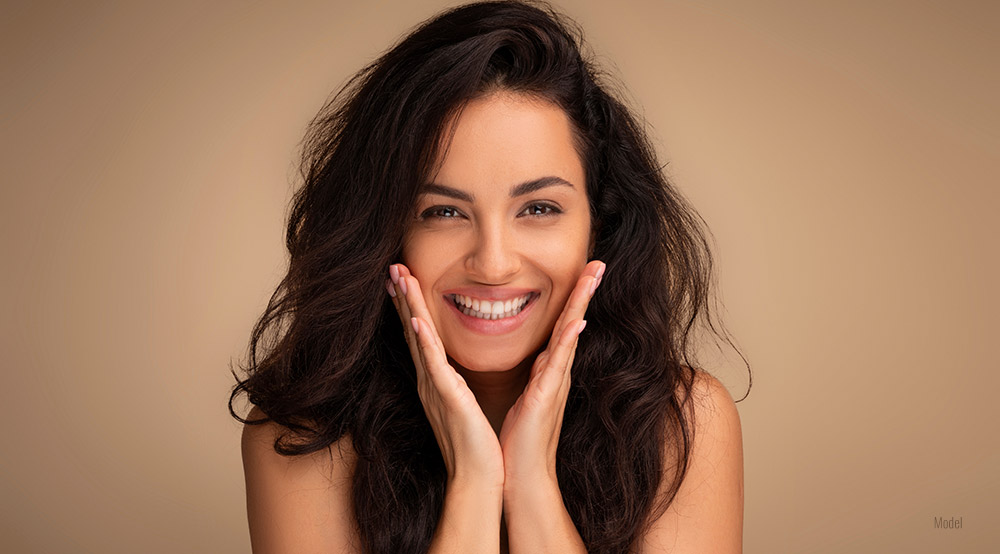 women wit big smile and both hands over her cheek. 